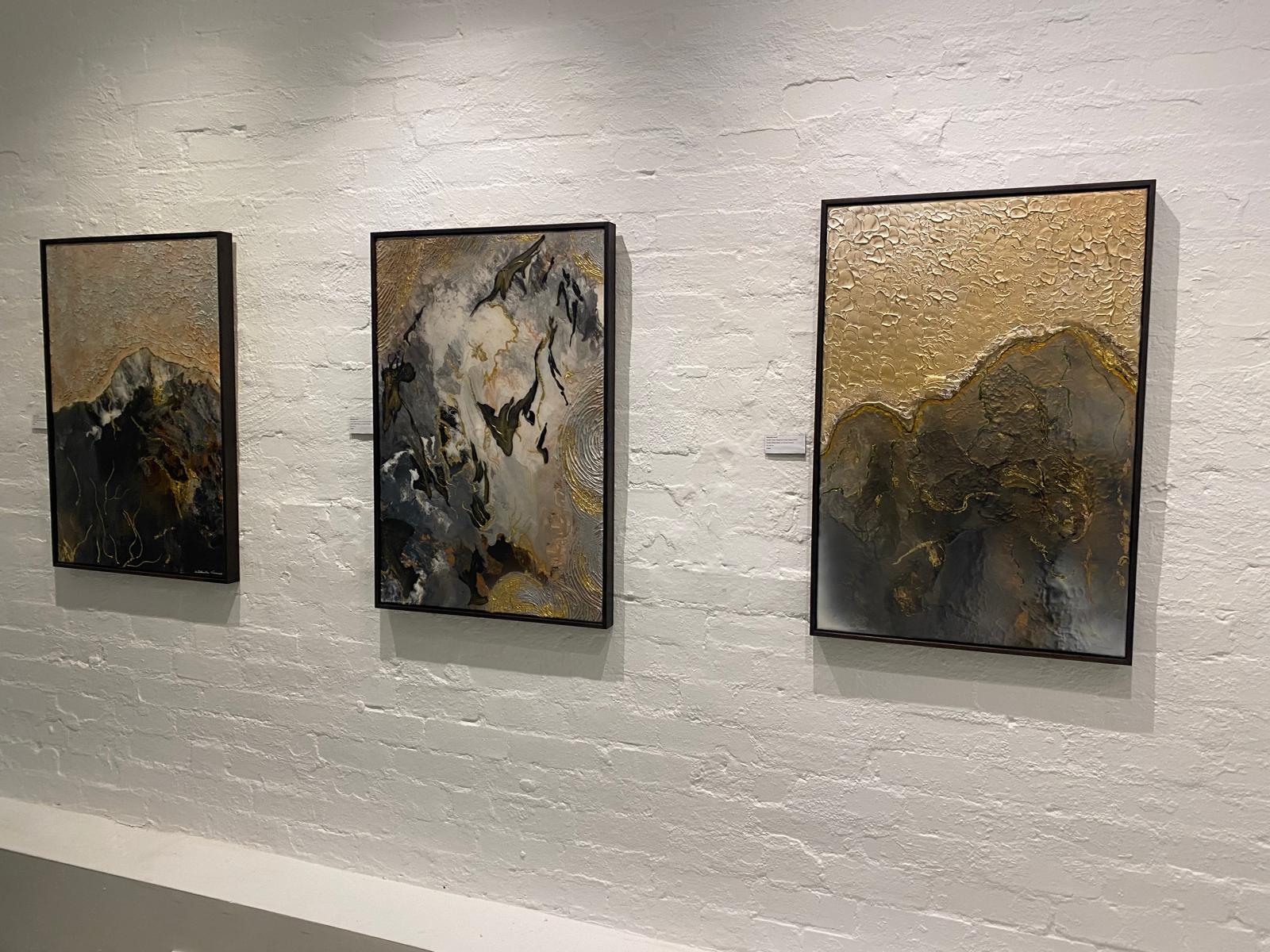 Three framed abstract works hung on a white brick gallery wall